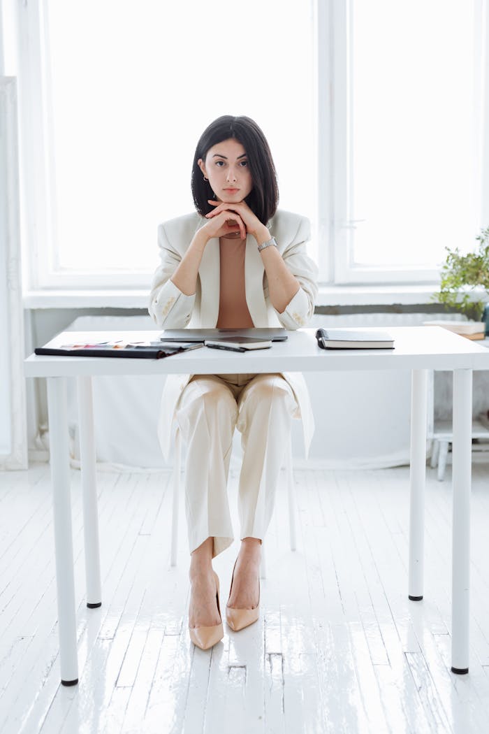 Elegant businesswoman in a white suit sitting at office desk, exuding confidence.